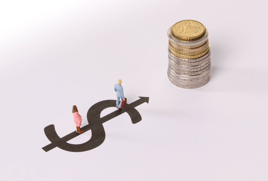 Man and Woman standing on dollar symbol pointing at stack of coins